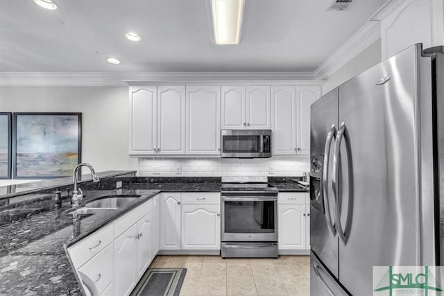 kitchen featuring appliances with stainless steel finishes, dark stone counters, white cabinets, ornamental molding, and sink