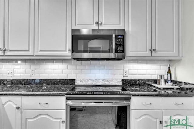 kitchen featuring appliances with stainless steel finishes, white cabinetry, dark stone counters, and backsplash