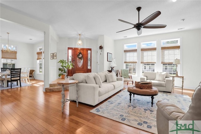 living room featuring ceiling fan with notable chandelier and light wood-type flooring