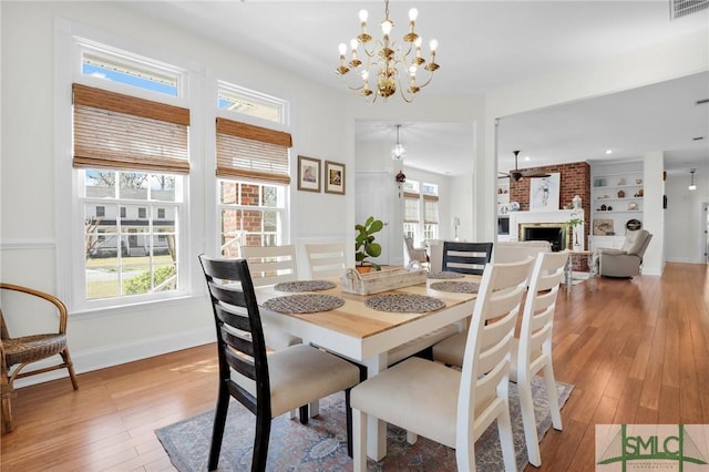 dining room with built in features, a brick fireplace, light hardwood / wood-style floors, and ceiling fan with notable chandelier