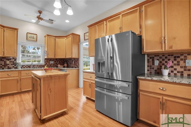 kitchen with a center island, light stone counters, light wood-type flooring, and stainless steel fridge with ice dispenser