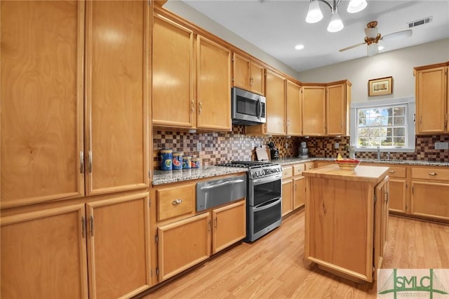 kitchen with a center island, light hardwood / wood-style floors, ceiling fan, appliances with stainless steel finishes, and decorative backsplash