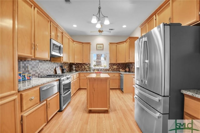 kitchen with appliances with stainless steel finishes, light stone counters, ceiling fan, pendant lighting, and a kitchen island