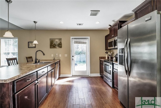 kitchen featuring appliances with stainless steel finishes, dark brown cabinets, wood-type flooring, decorative light fixtures, and sink