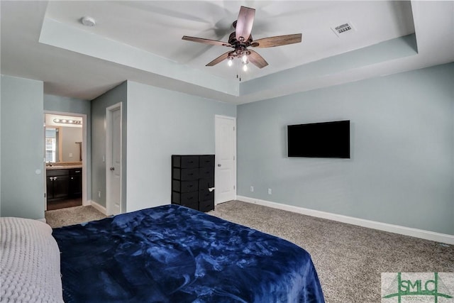 bedroom featuring a tray ceiling, ensuite bath, carpet floors, and ceiling fan