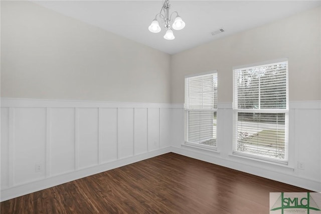 empty room with a wainscoted wall, wood finished floors, visible vents, and an inviting chandelier