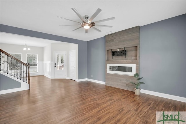 unfurnished living room with a large fireplace, baseboards, stairway, and dark wood-style floors