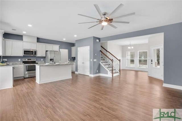 kitchen featuring white cabinets, a kitchen island, appliances with stainless steel finishes, open floor plan, and wood finished floors