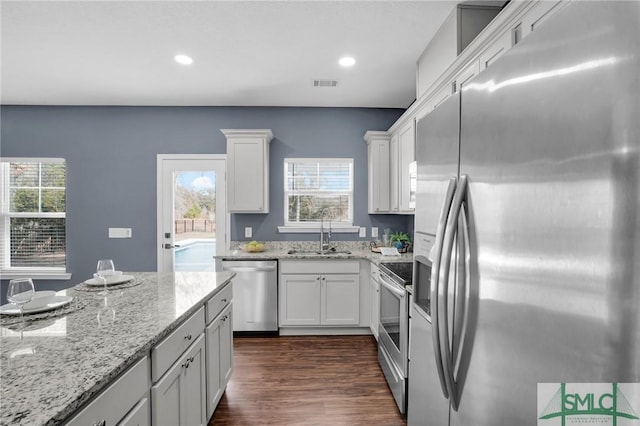 kitchen featuring visible vents, light stone counters, stainless steel appliances, white cabinetry, and a sink