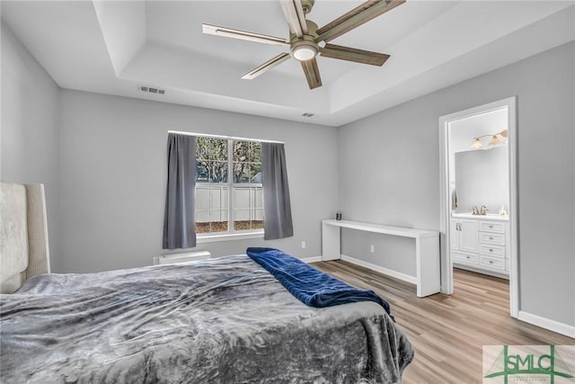 bedroom with ensuite bathroom, light hardwood / wood-style floors, a tray ceiling, and sink