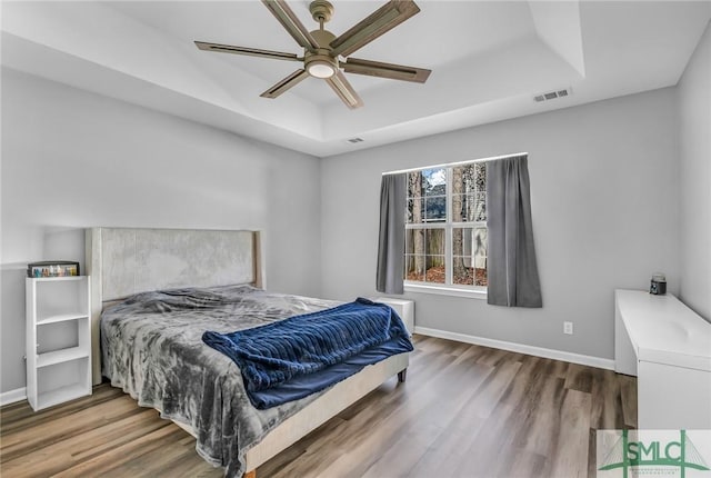 bedroom with ceiling fan, a raised ceiling, and hardwood / wood-style floors