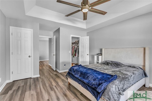 bedroom with a spacious closet, a raised ceiling, a closet, and hardwood / wood-style floors