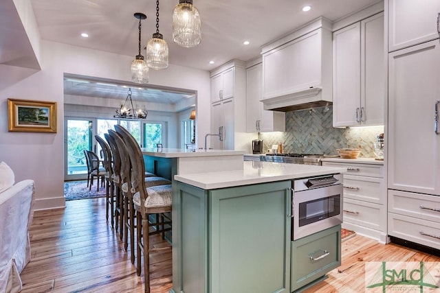 kitchen with an island with sink, white cabinets, stainless steel microwave, pendant lighting, and green cabinetry