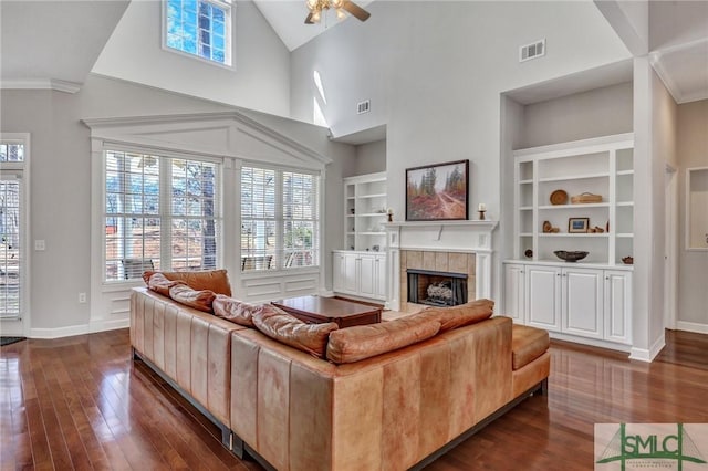 living room with dark wood-type flooring, a tiled fireplace, high vaulted ceiling, and built in shelves