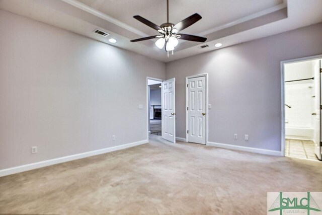 unfurnished bedroom with light carpet, ceiling fan, a tray ceiling, and connected bathroom