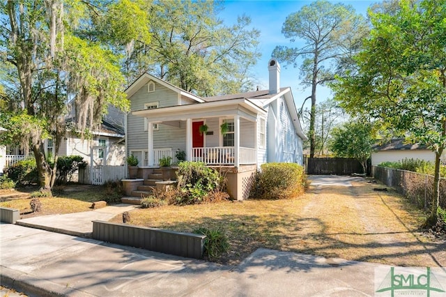 view of front of home with driveway, a chimney, a porch, and fence