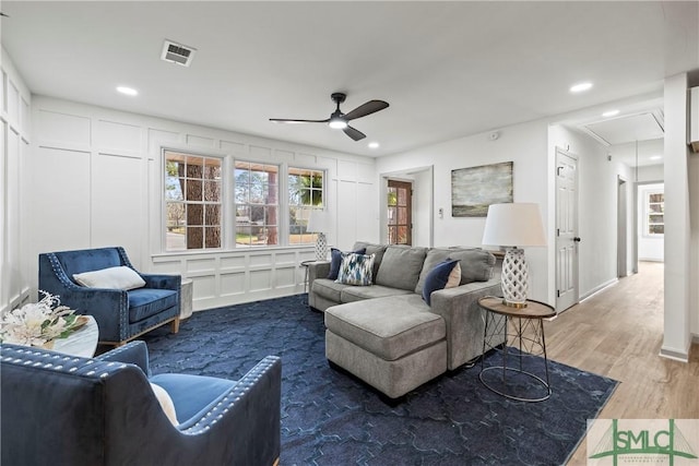 living room featuring ceiling fan, attic access, wood finished floors, a decorative wall, and visible vents