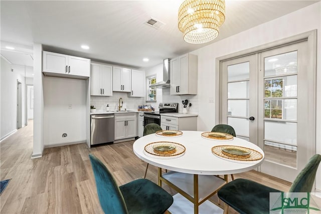 kitchen with wall chimney exhaust hood, stainless steel appliances, white cabinets, and light countertops