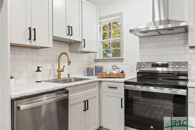 kitchen featuring wall chimney exhaust hood, stainless steel appliances, decorative backsplash, white cabinetry, and a sink