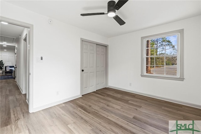 unfurnished bedroom featuring attic access, a closet, light wood finished floors, baseboards, and a ceiling fan