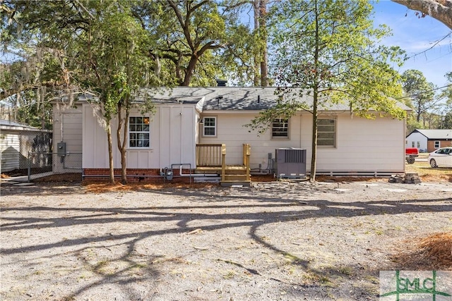 back of property with central air condition unit, board and batten siding, fence, and roof with shingles