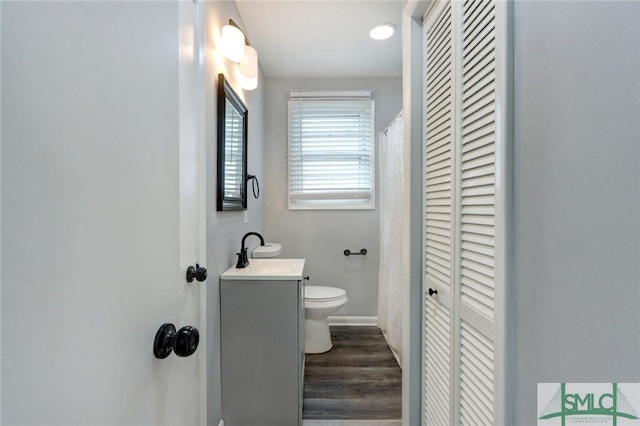 bathroom featuring wood finished floors, vanity, baseboards, toilet, and a closet