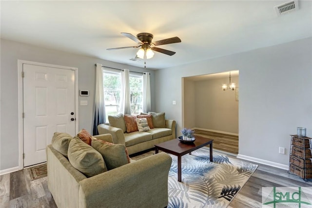 living area featuring ceiling fan with notable chandelier, visible vents, baseboards, and wood finished floors