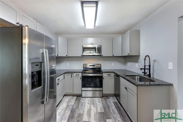 kitchen with dark stone countertops, a sink, appliances with stainless steel finishes, and light wood-type flooring