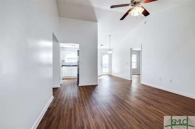 unfurnished living room featuring dark wood-style floors, a ceiling fan, baseboards, lofted ceiling, and a textured ceiling