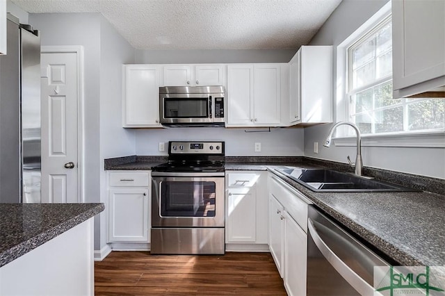 kitchen with stainless steel appliances, white cabinets, a sink, a textured ceiling, and dark wood finished floors