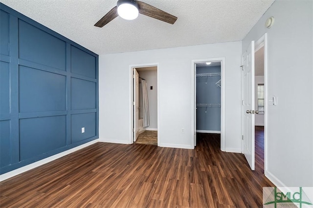 unfurnished bedroom featuring a ceiling fan, a walk in closet, a textured ceiling, dark wood-style flooring, and a closet