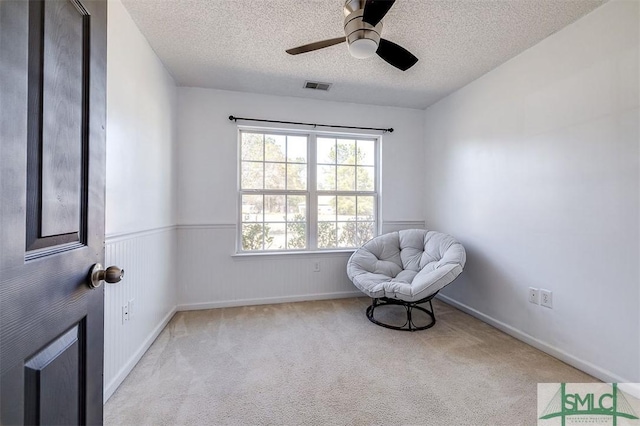 sitting room featuring a wainscoted wall, visible vents, light carpet, and a textured ceiling