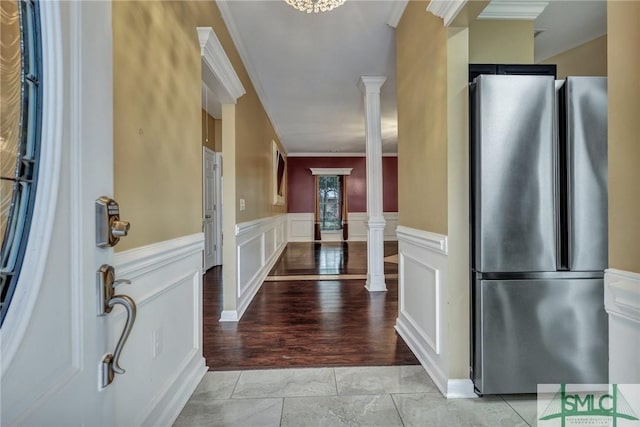 entrance foyer with crown molding, decorative columns, a decorative wall, light wood finished floors, and a wainscoted wall