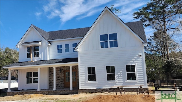 rear view of property with fence, brick siding, roof with shingles, board and batten siding, and a porch