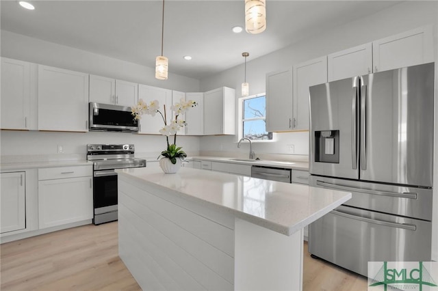 kitchen with appliances with stainless steel finishes, a kitchen island, white cabinetry, and decorative light fixtures