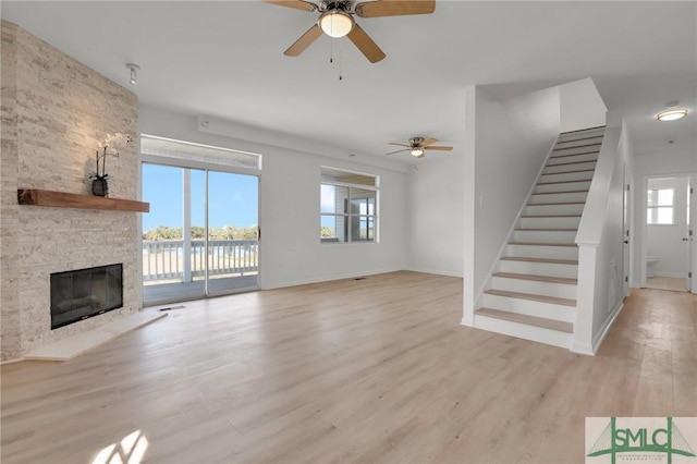 unfurnished living room with visible vents, a ceiling fan, stairway, a stone fireplace, and light wood-style floors