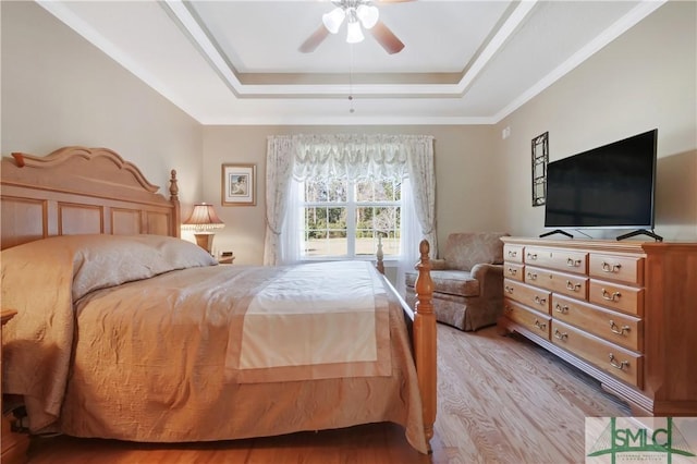 bedroom with light wood-style floors, a raised ceiling, and a ceiling fan