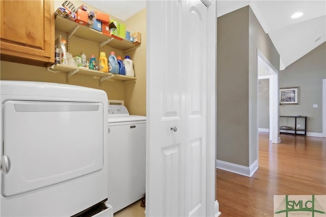 clothes washing area featuring cabinet space, light wood-style flooring, baseboards, and washing machine and clothes dryer