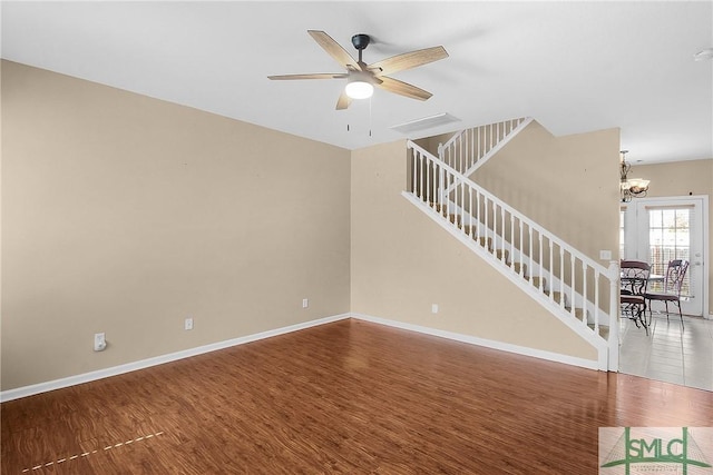 unfurnished living room with ceiling fan with notable chandelier, stairway, baseboards, and wood finished floors