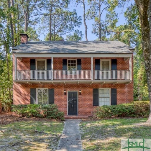 view of front of home featuring a chimney, brick siding, and a balcony