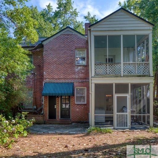 back of house featuring a sunroom, brick siding, and a chimney