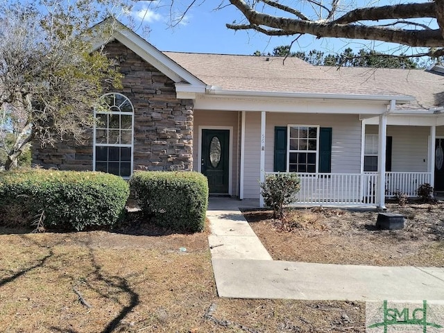 view of front of property with stone siding, covered porch, and roof with shingles