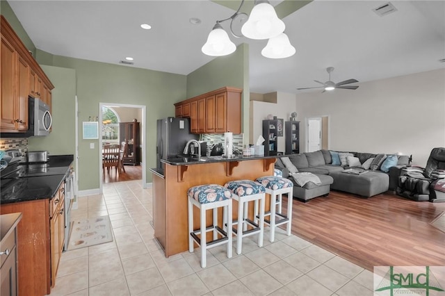 kitchen with visible vents, brown cabinetry, stainless steel microwave, open floor plan, and backsplash