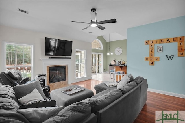 living area featuring lofted ceiling, a tile fireplace, dark wood-style flooring, visible vents, and baseboards