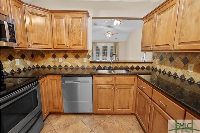 kitchen featuring brown cabinets, dark stone countertops, stainless steel appliances, and a sink