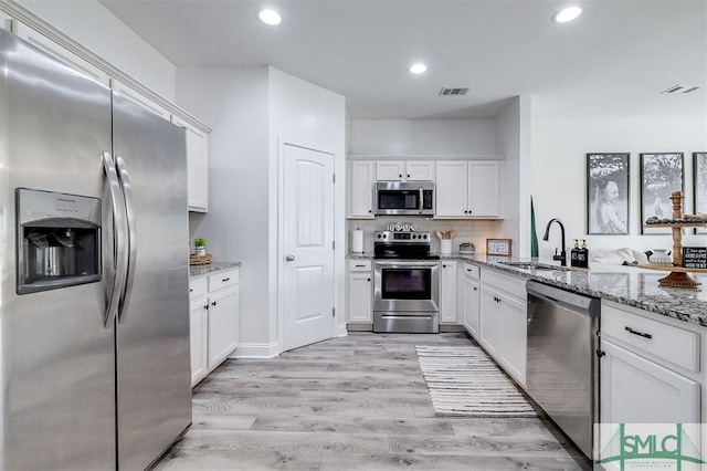 kitchen featuring visible vents, light stone counters, stainless steel appliances, white cabinetry, and a sink