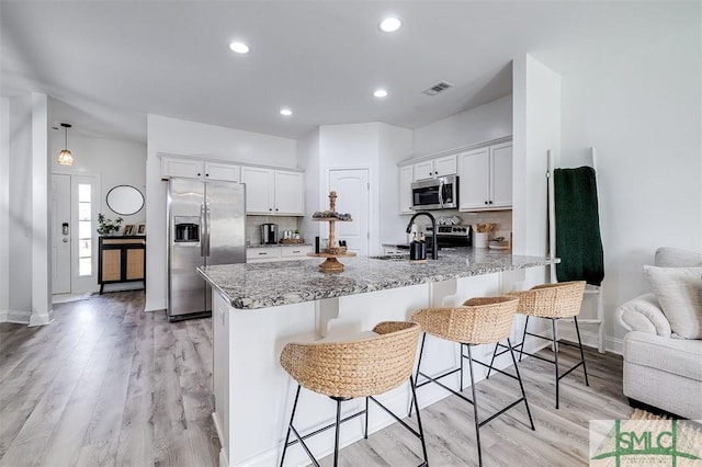 kitchen with stainless steel appliances, visible vents, light wood-style floors, white cabinets, and a sink