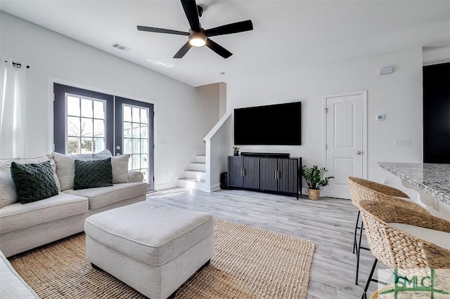 living room with visible vents, a ceiling fan, stairway, french doors, and light wood-type flooring