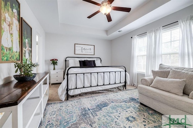 carpeted bedroom featuring ceiling fan, a raised ceiling, and visible vents