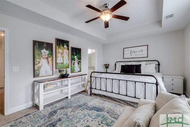 carpeted bedroom with visible vents, baseboards, a raised ceiling, ceiling fan, and ensuite bathroom